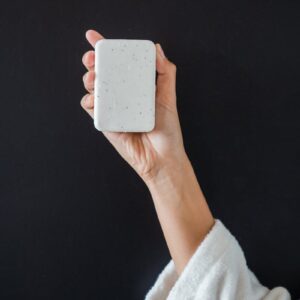 Close-up of a hand in a robe holding a bar of white soap against a black background, symbolizing cleanliness.